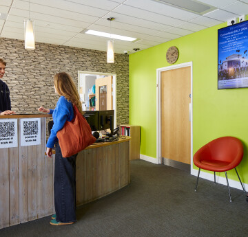 Myfyriwr yn siarad ag aelod o staff yn y dderbynfa i gael cymorth llety