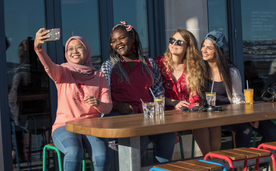 Group of students taking a selfie sat outside a cafe